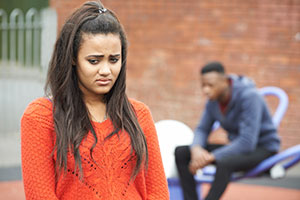 A girl looking sad with a boy in the background.